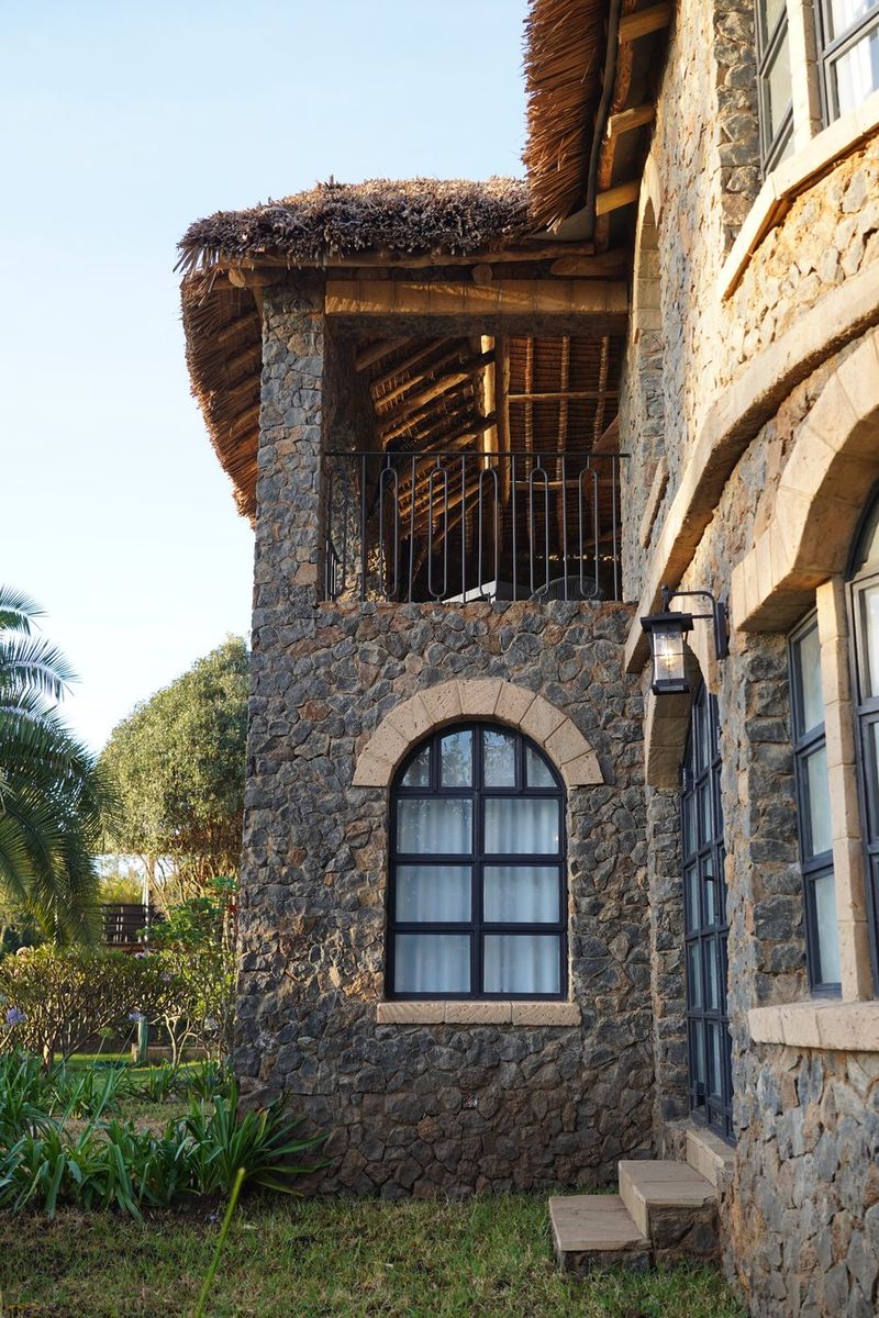 A stone tower corner of O'Leleshwa under thatch, an arched window and a wall lantern lit in warm evening light, agapanthus below.