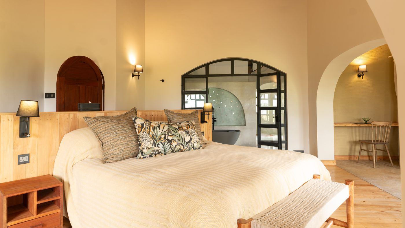 A bedroom looking through black steel-framed doors to a bathroom with a sage terrazzo arch and grey tub, a desk nook at the right.