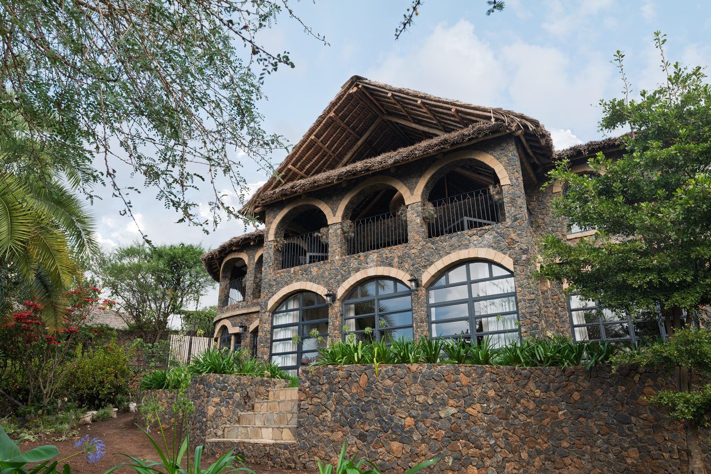 The O'Leleshwa stone facade from below: an arched loggia under thatch, an agapanthus terrace and a stone retaining wall.