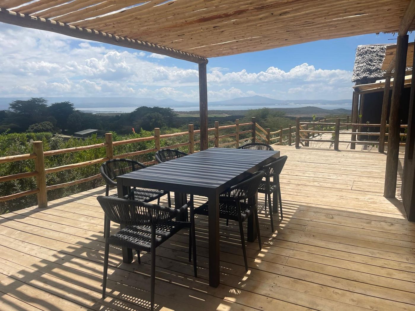 O'Lerai's deck under its pole pergola — the black table and rope chairs, the pole rail, Lake Naivasha and the Rift hills beyond.
