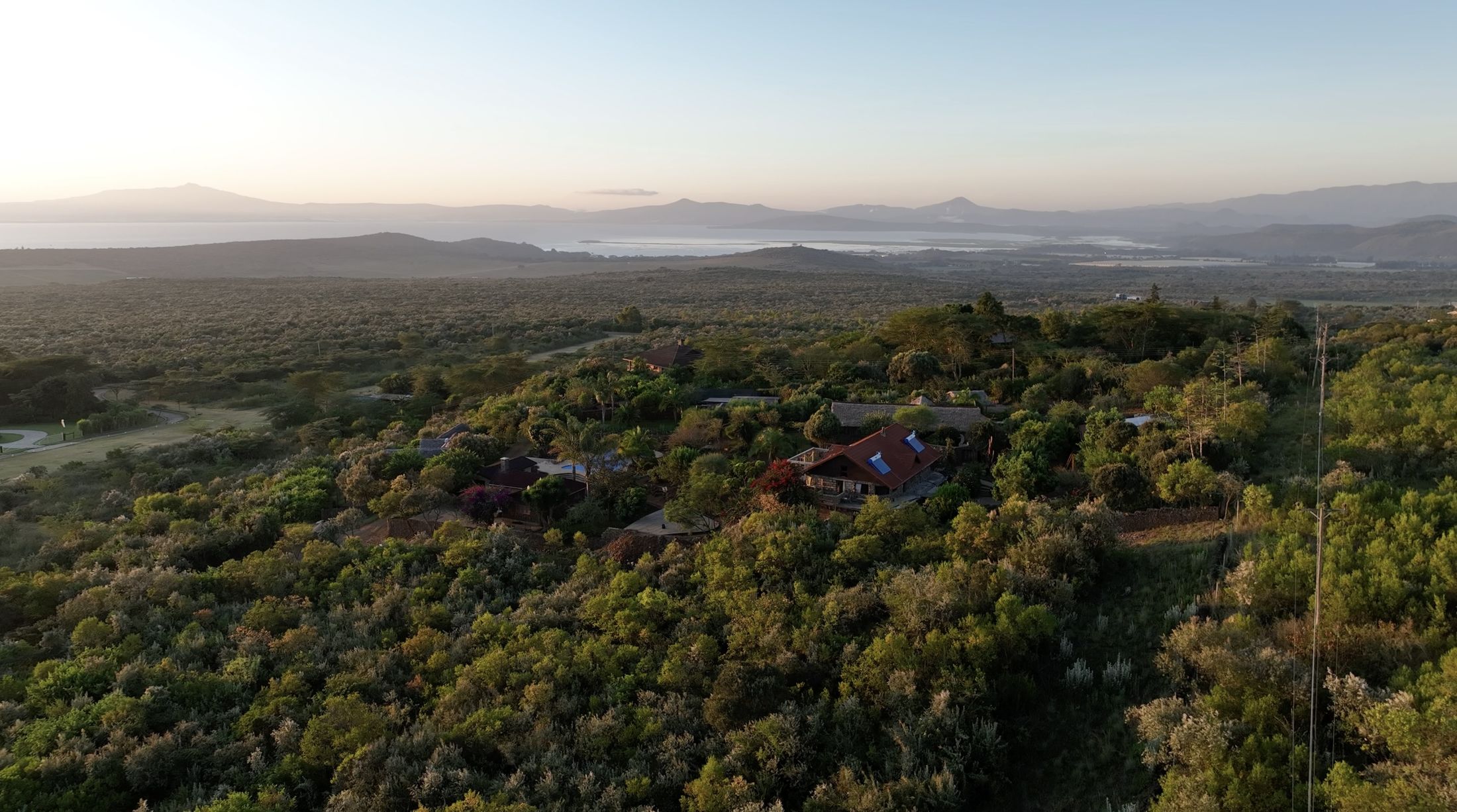 A dawn aerial of the hilltop estate in silver-green leleshwa scrub, Lake Naivasha and hazy Rift hills beyond.